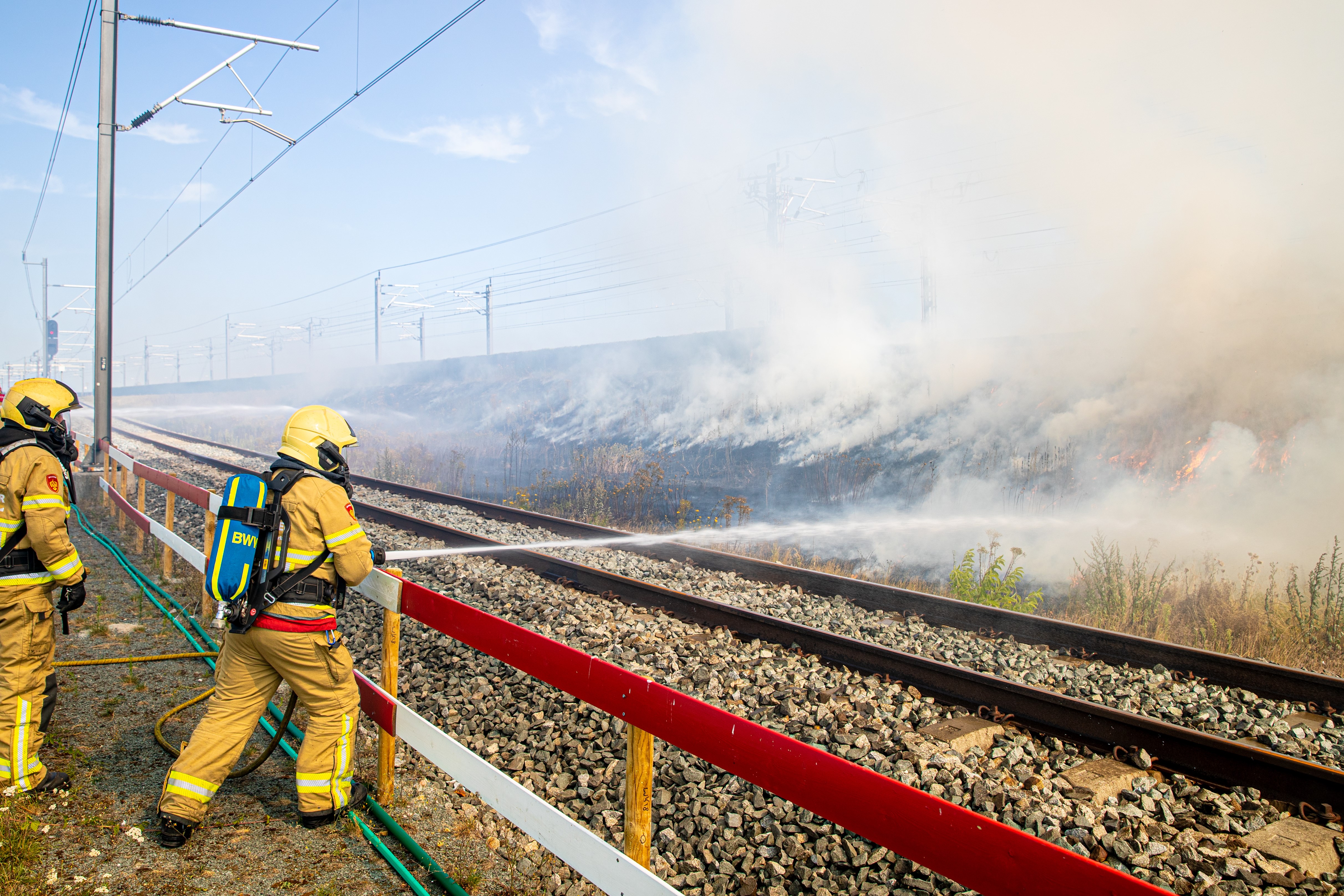 Afbeelding met een brandweerman die een spoorberm blust.